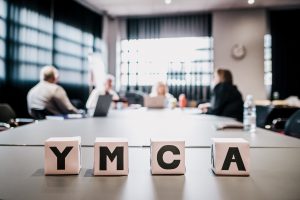 YMCA staff, out of focus behind white blocks spelling YMCA in black letter. 