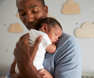 A male parent cuddles a sleeping baby