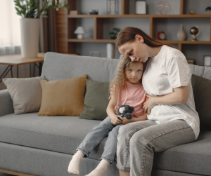 A young mum cuddling her daughter on a couch. Both are sad and upset. 