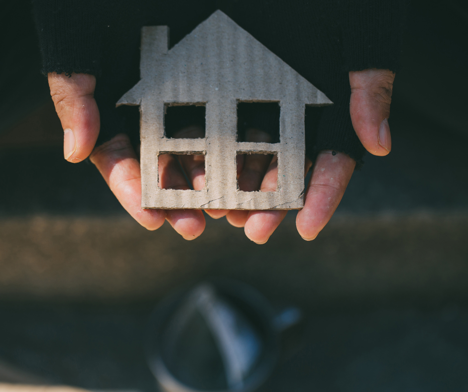 Hands wearing fingerless gloves hold out a cardboard cut-out of a house.