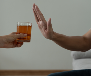 A hand refusing a glass of an alcoholic spirits. 