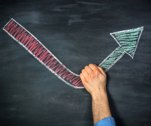 A chalkboard showing a red downward arrow being intercepted by a hand, changing it to a green, upward arrow. 