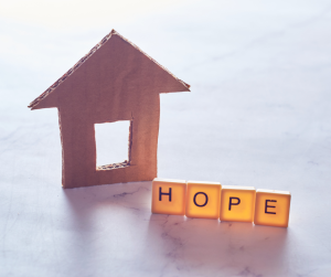 A small cardboard house next to Scrabble letters spelling out Hope