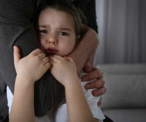 A young girl holding on to a parent's arm for safety. 