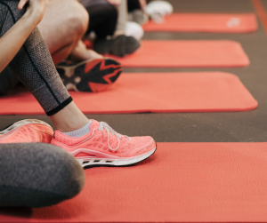 A close up of female feet in training shoes, resting on a pink yoga mat. 