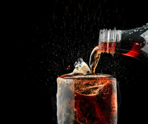 A glass of cola being poured into a full to the brim glass against a black background