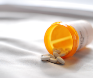 An open prescription medication container, with pills spilling on to a white sheet. 