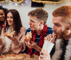 Two males and two females eating pizza while wearing tinsel. 