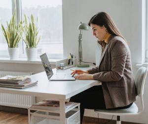 A dark-haired female working at her laptop in a well lit office. 