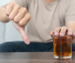 A close of a male covering his glass of alcohol with one hand and giving a thumbs down with the other. Refusing to accept more alcohol. 