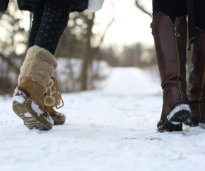 Close up of two women walking through snow in winter boots. 