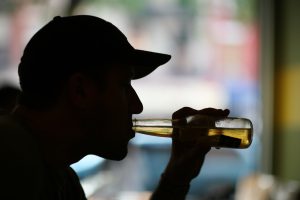 Silhouette close-up of a cap-wearing meal drinking a bottle of beer. 