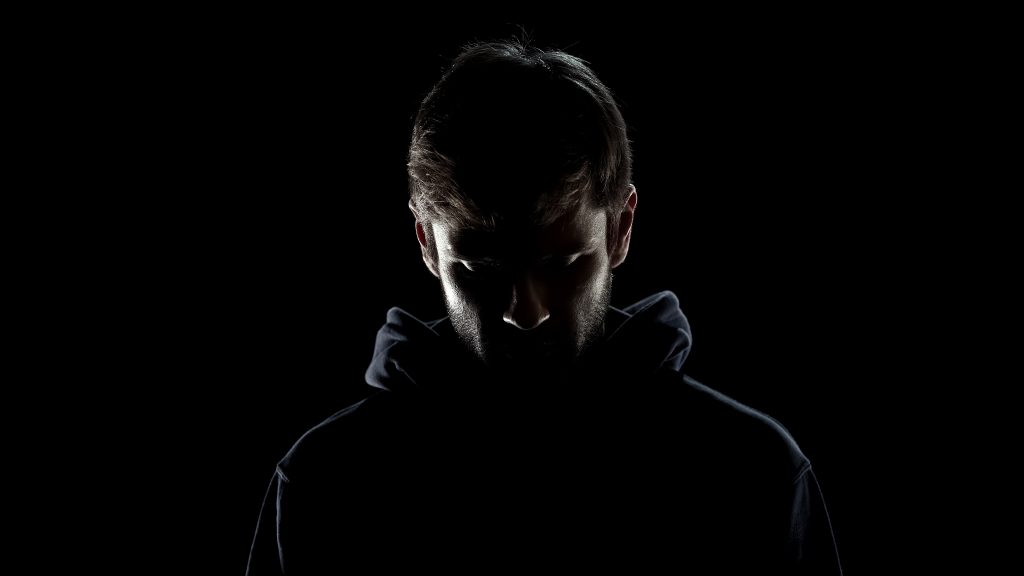 Silhouette of a male in a hooded jacket looking regretful. 