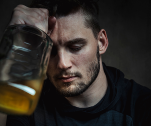 A depressed looking man, clutching a bottle of alcohol. 