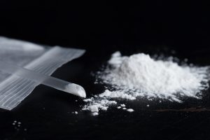 A close up of an open bag of ketamine (white powder) near a short straw for ingesting. 