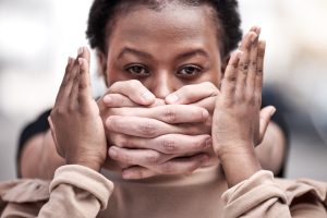 A Black Woman being silenced with hands around her mouth from behind. 