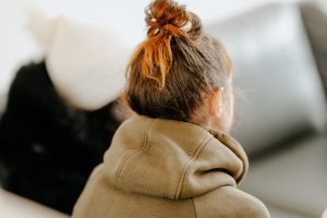 Rear view of female wearing a light brown hoodie with hair in a top knot. 